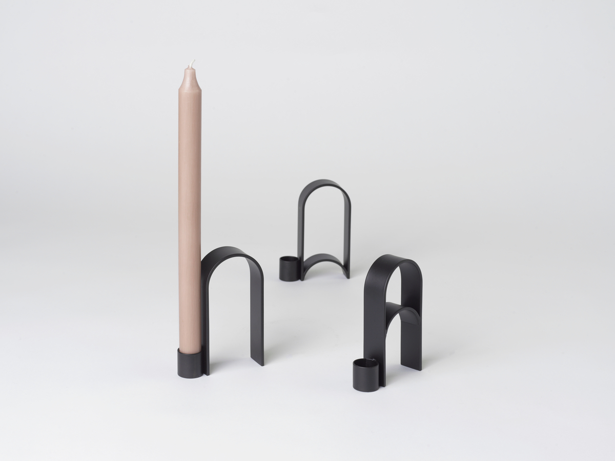 Ein modernes Design-Kerzenhalter-Set aus Metall namens 'Arch' Vol.10 in Schwarz. Der Kerzenhalter verfügt über einen eleganten und minimalistischen Bogenstil. Eine beige Kerze ist in einem der Kerzenhalter platziert. Geeignet für eine Vielzahl von Anlässen, insbesondere als stilvolle Inneneinrichtung.