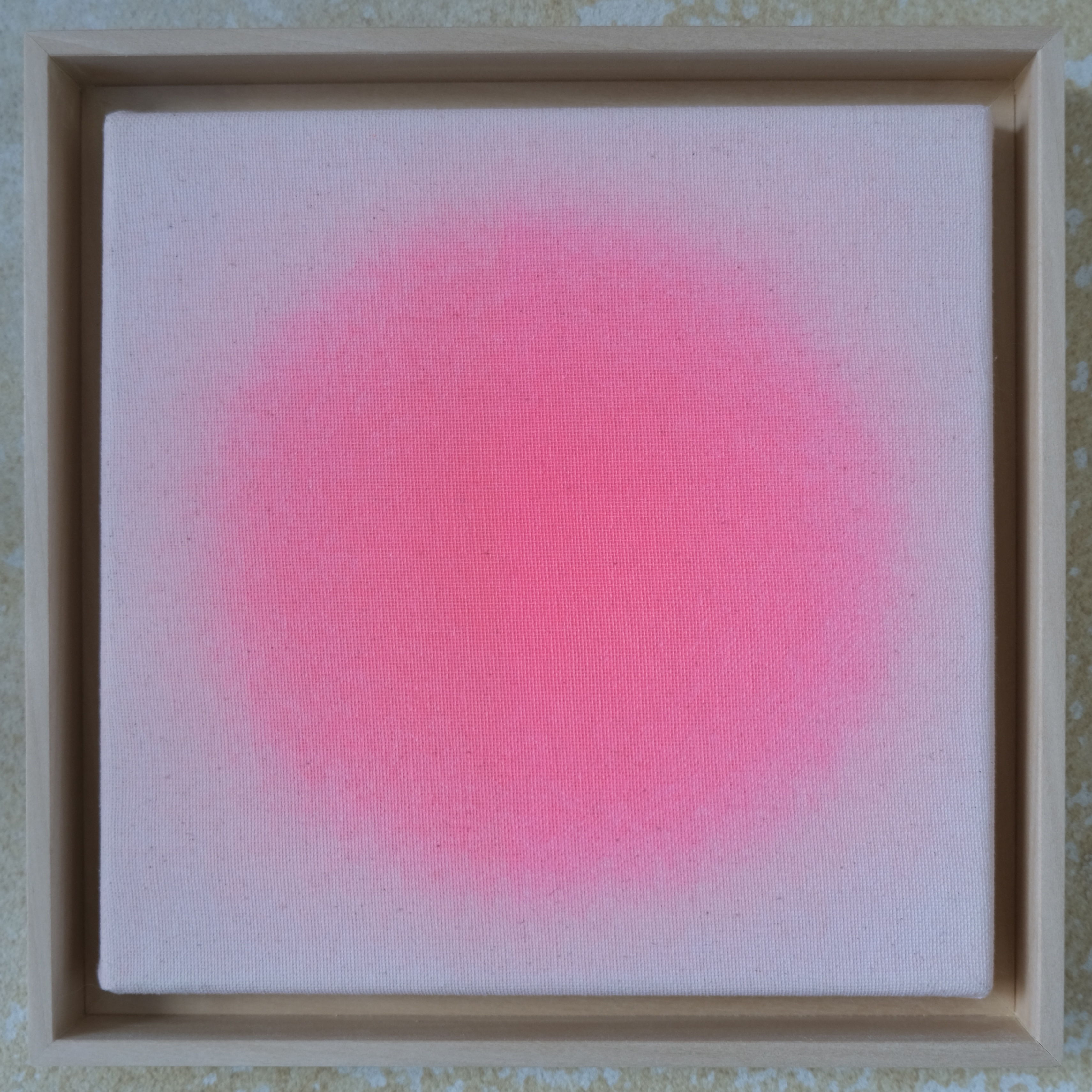Quadratisches Kunstwerk »Sorbet« mit zartem, strahlendem Pinkverlauf auf ungebleichter Leinwand in Naturbeige. Rund um das Pink wirkt die Farbe zum Rand hin weicher. Das Bild ist in einem schlichten, hellen Lindenholzrahmen gefasst und auf einer Natursteinwand platziert.