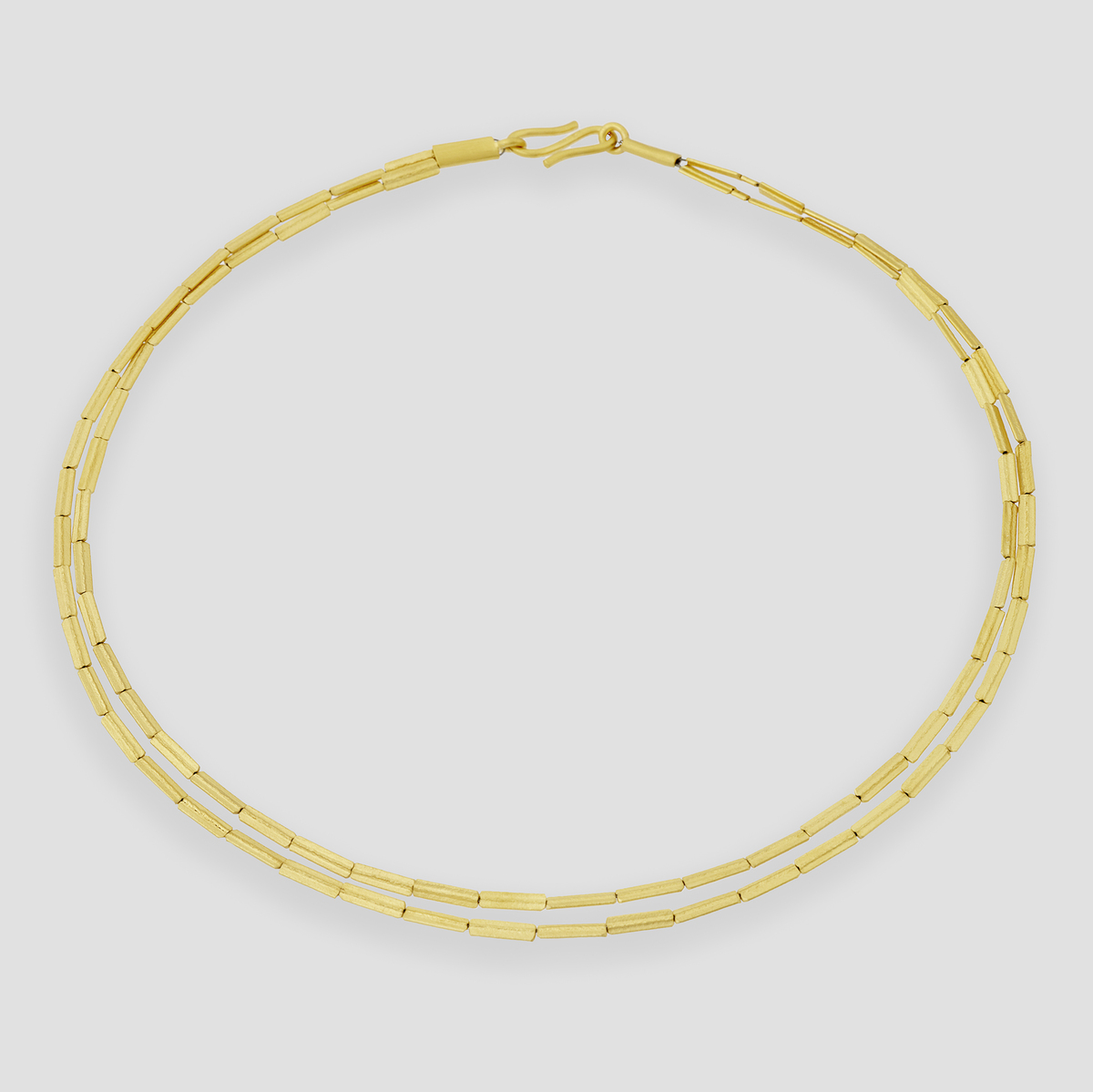 Fotografie eines eleganten, zweireihigen Colliers in Halmketten-Optik, aus silbernem Metall gefertigt und mit feinem Gold überzogen. Das Schmuckstück liegt auf hellem, neutralem Untergrund und wirkt modern sowie hochwertig verarbeitet.