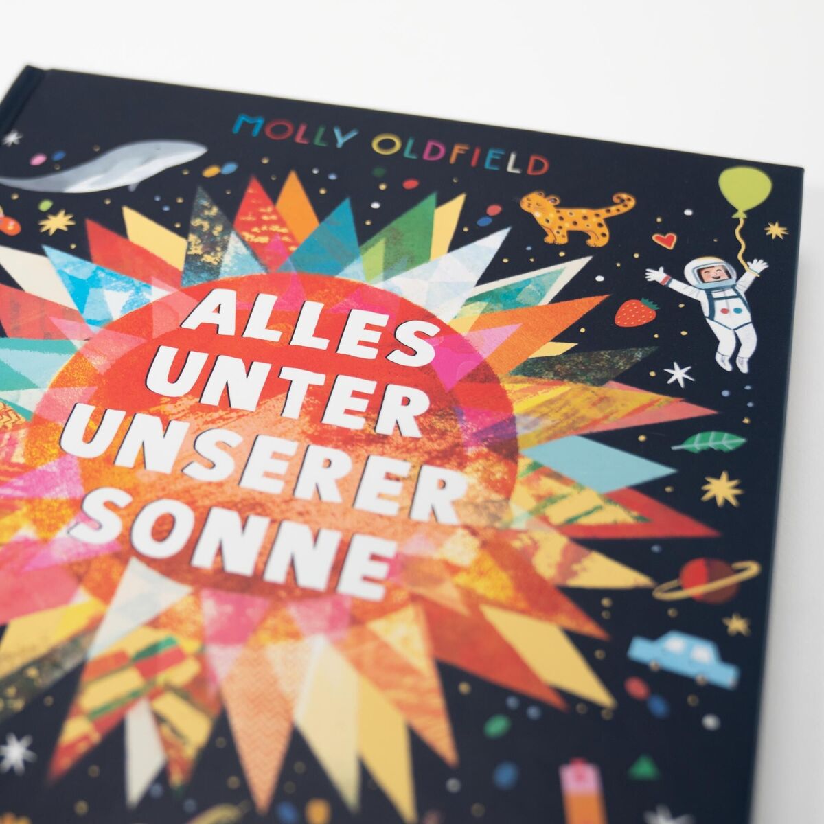 Das Buch 'Alles unter unserer Sonne' von Molly Oldfield zeigt eine farbenfrohe Abbildung der Sonne im Mittelpunkt und diverse Elemente aus der Wissenschaft und Natur, wie einen Astronauten, ein Tiger und einen Wal, auf schwarzem Hintergrund.