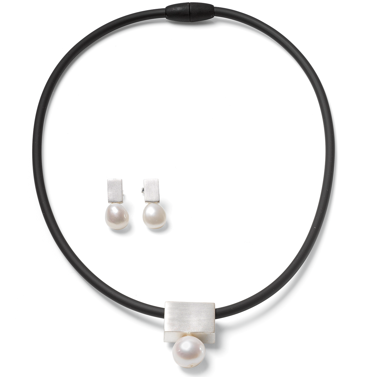 Das Bild zeigt das Schmuckset "Mother of Pearl" von Ars mundi: eine schwarze Kautschukkette mit einem rechteckigen, versilberten Anhänger und runder weißer Perle, dazu passende Ohrringe mit silbernem Stecker und hängender weißer Perle. Das Design ist elegant und modern.