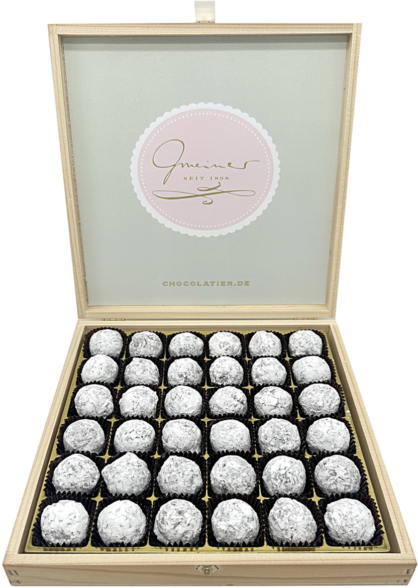 Elegante Holzbox mit 36 Champagnertrüffeln von Gmeiner. Die Pralinen sind mit weißem Puder bestäubt und einzeln in goldenen Papierförmchen angeordnet. Im Deckel der Box erscheint das Gmeiner-Logo auf mintgrünem Hintergrund. Hochwertiges Präsent für Genießer.