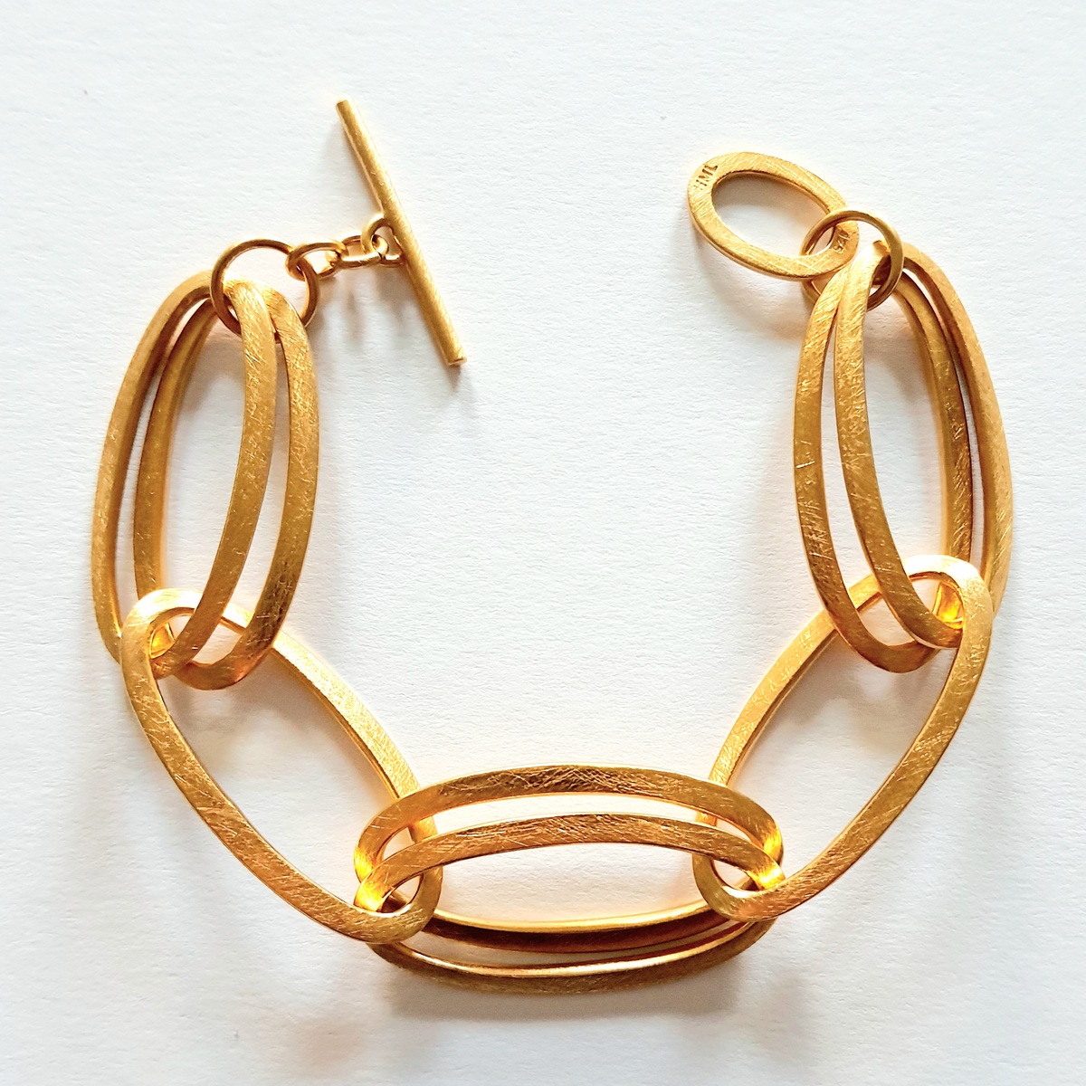 Ein elegantes, goldenes Armband bestehend aus miteinander verbundenen ovalen Gliedern mit einem T-Verschluss, das auf einem weißen Hintergrund fotografiert wurde.