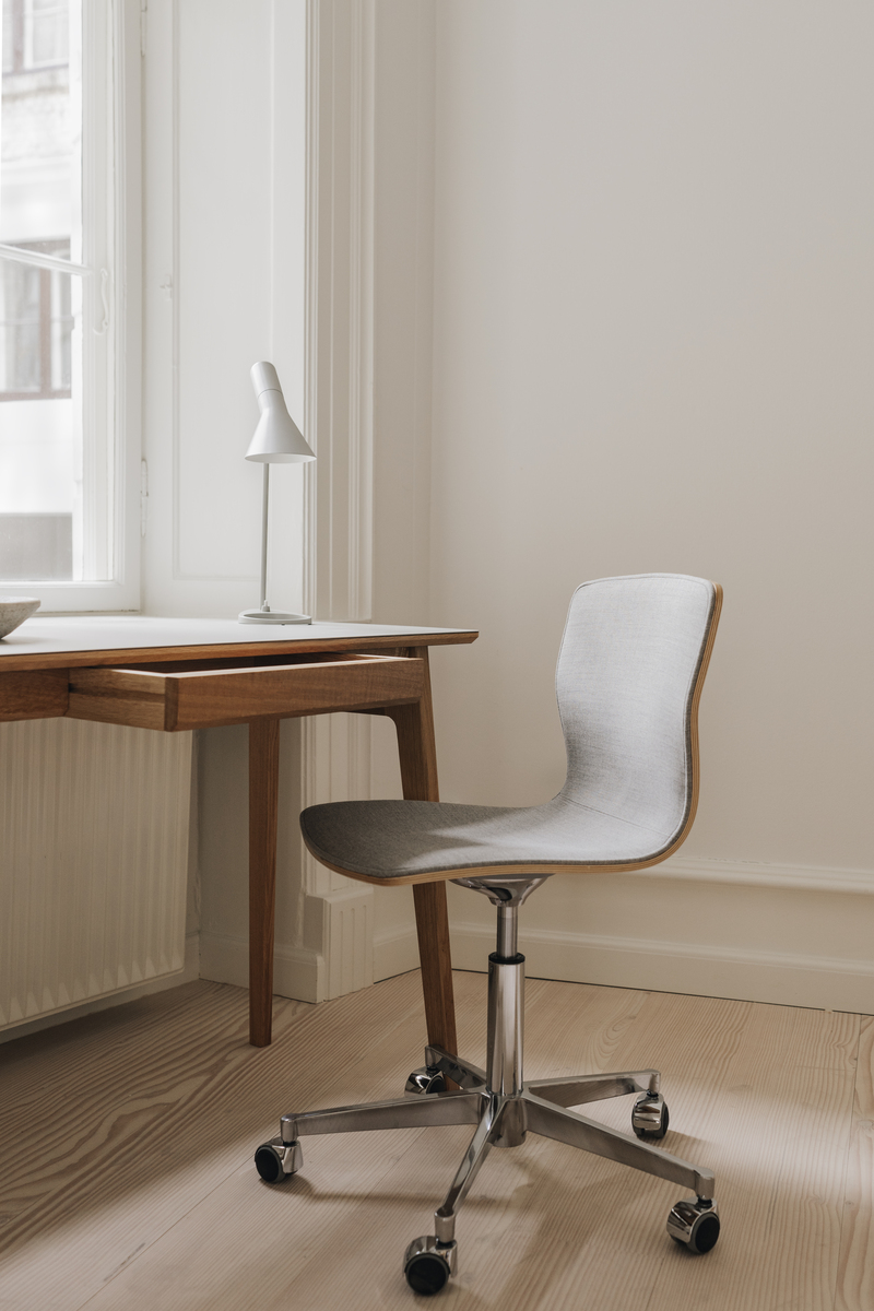 Ein moderner Schreibtisch aus Eiche mit minimalistischen Design, dazu passend ein hellgrauer Bürostuhl auf Rollen vor einem großen Fenster.