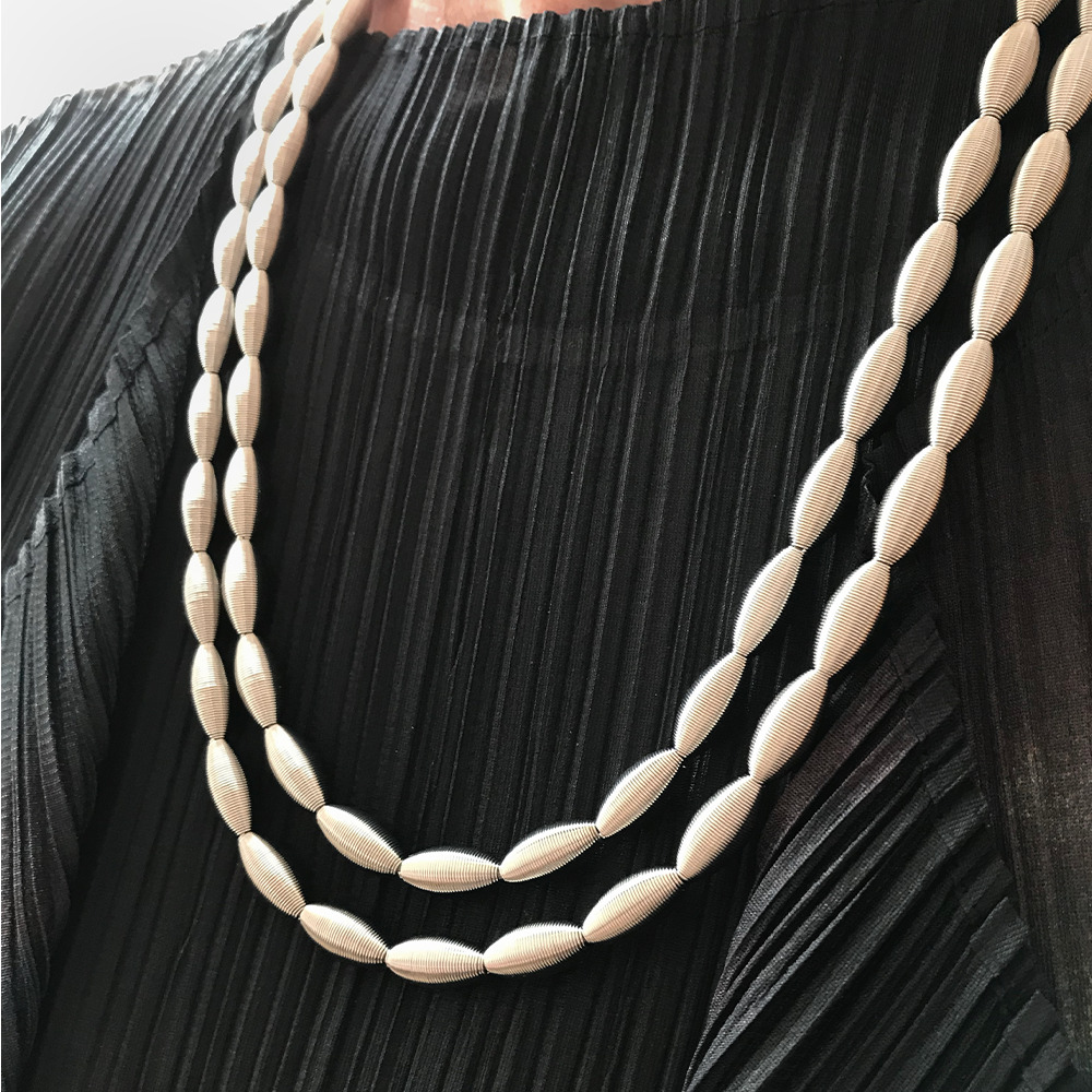 Silbernes Collier »Lotusmall« mit zwei Reihen ovaler Perlen, getragen auf einem schwarzen, plissierten Oberteil. Lüsternde, elegante Halskette, passend zu festlicher oder formeller Kleidung.
