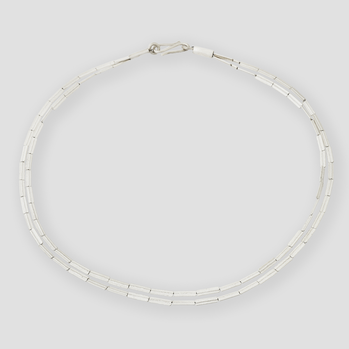 Nahaufnahme einer filigranen, silberfarbenen Halmkette mit geprägten Elementen auf hellem, neutralem Hintergrund. Das Collier wirkt elegant und zeitlos, ideal als Schmuckstück für besondere Anlässe oder den täglichen Gebrauch.