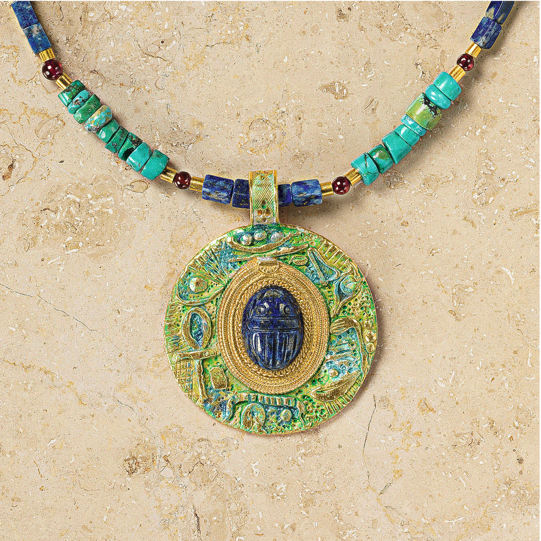 Detailreiche Nahaufnahme des Colliers »Scarabeo« von Petra Waszak für Ars mundi: Der runde Anhänger zeigt einen zentralen Skarabäus aus tiefblauem Lapis, umgeben von türkisen, blauen und roten Steinen sowie glanzvollen Elementen aus 24 Karat vergoldetem Messing. Die Kette ist edel und hochwertig verarbeitet.
