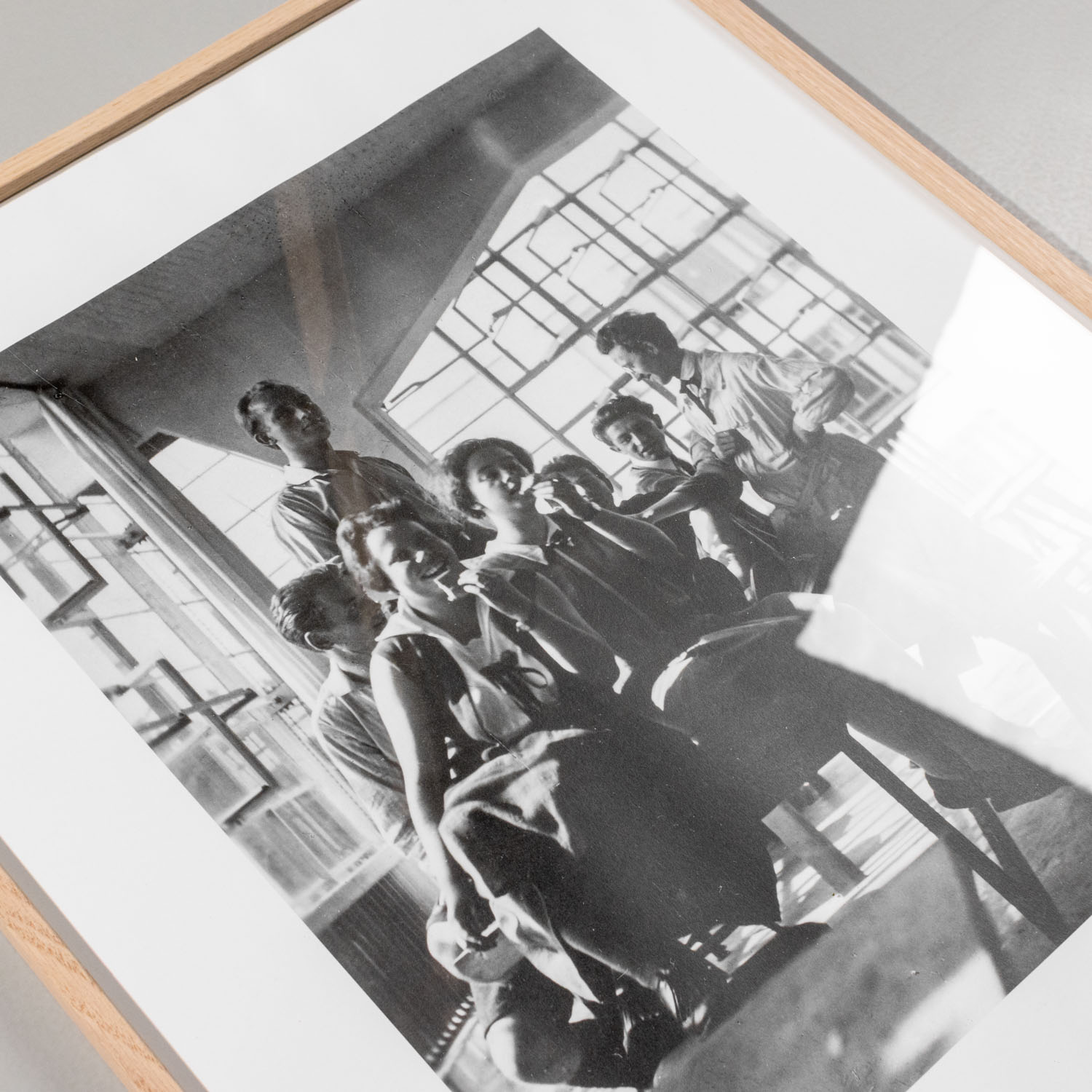 Schwarzweißfotografie in einem Holzrahmen zeigt eine Gruppe von Menschen im historischen Bauhaus Archiv Berlin im Jahr 1928. Das Bild ist minimalistisch und von moderner Architektur umgeben, ideal für Kunstliebhaber und Freunde der Designgeschichte.