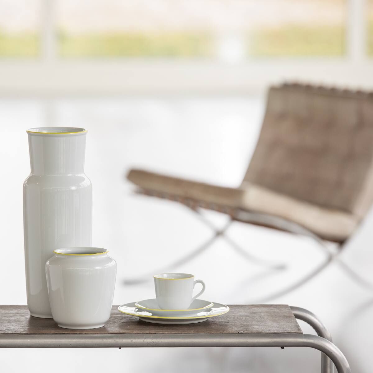 Ein elegantes Arrangement der ZEIT-Sonderedition »Wagenfeld Vase 639/14« von Fürstenberg auf einem Tisch. Die weiße Vase und andere weiße Keramikgegenstände sind vor einem unscharfen Hintergrund platziert.