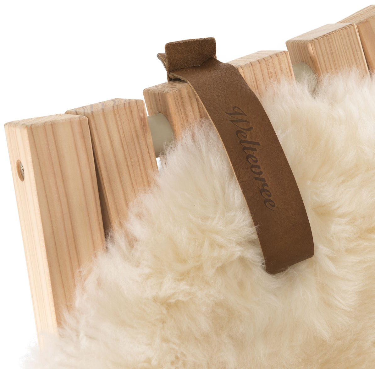 Ein cremeweißes Schafsfell mit einer braunen Lederschlaufe liegt dekorativ über einer naturbelassenen Holzlehne. Das Bild vermittelt ein Gefühl von Gemütlichkeit und Wärme, ideal als Wohnaccessoire.