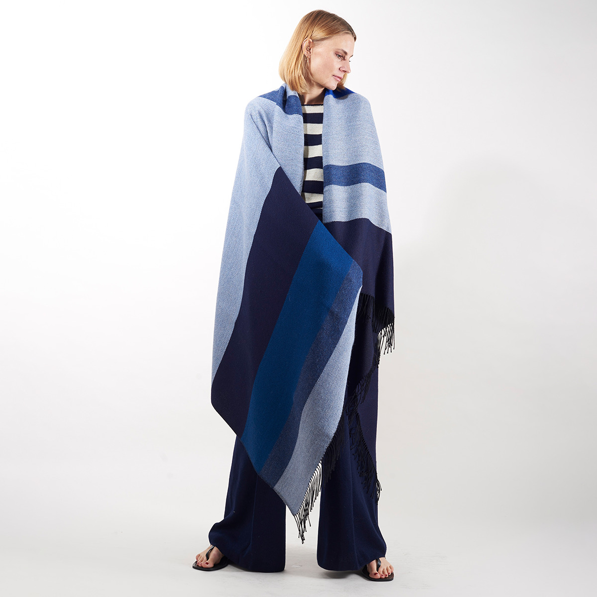 Person mit Cape „Shades of Blue“ aus der ZEIT-Jubiläumsedition. Das Cape hat verschiedene Blautöne und schwarze Fransen an den Enden. Es ist modebewusst und stilvoll, geeignet für Frauen.