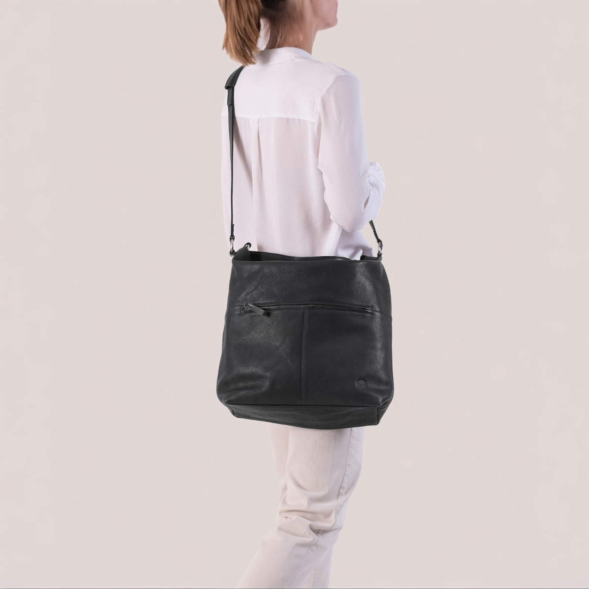 Eine elegante, schwarze Beuteltasche mit Schulterriemen, getragen von einer Person in heller Kleidung. Die Tasche hat ein minimalistisches Design und wirkt modern und funktional.