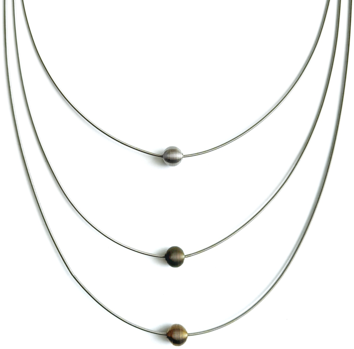 Dreilagige Halskette mit drei runden Perlen in Silber und Gold. Jeder Strang hat eine einzelne schlichte Perle, die auf dünnen, silberfarbenen Ketten hängt. Die Kette ist minimalistisch und elegant gestaltet.