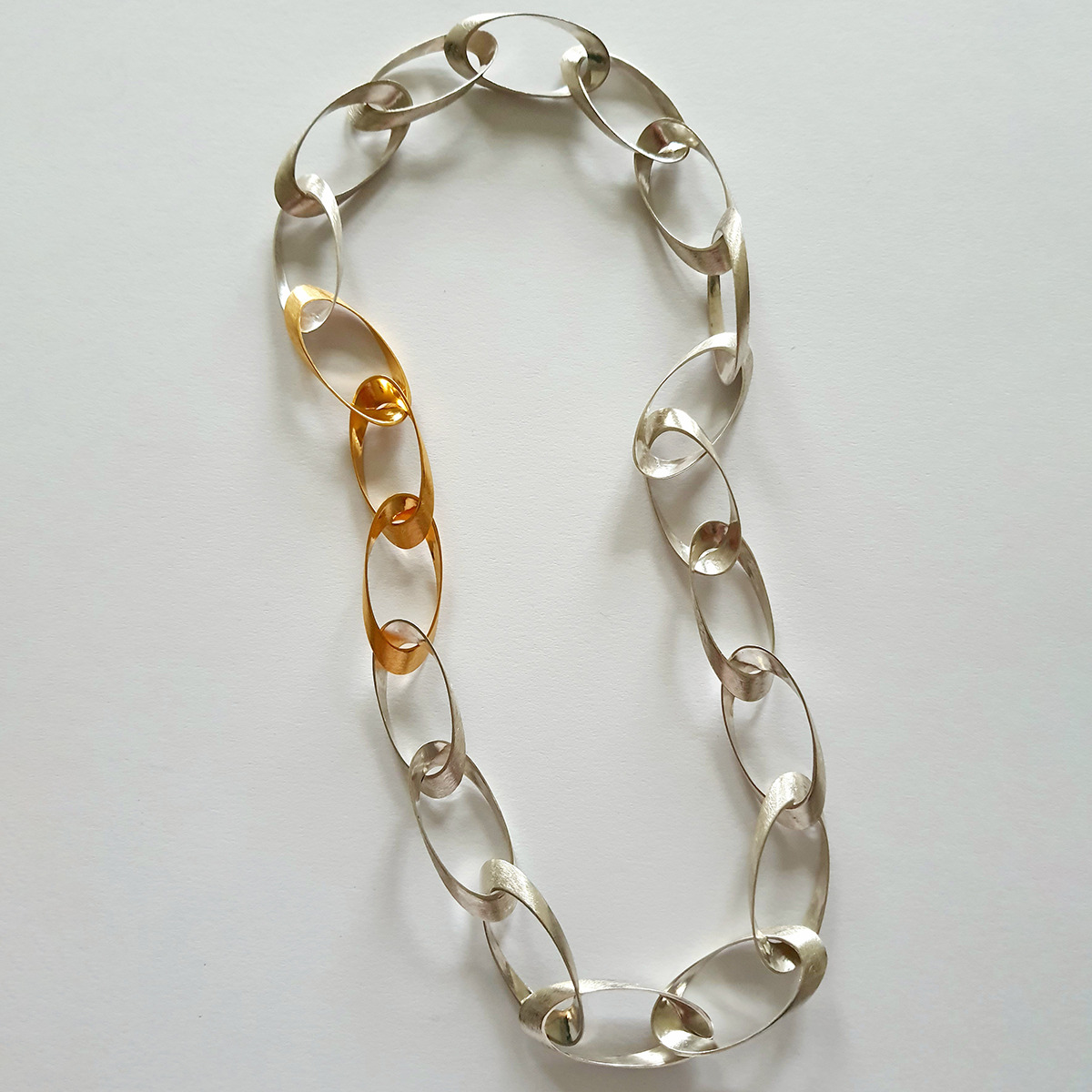 Edles Collier »Standing Ovations« der Marke HML Berlin aus 925er Silber und feingoldplattierten Elementen, bestehend aus handgefertigten ovalen Gliedern in Silber und Gold. Das Schmuckstück liegt auf hellem Untergrund und wirkt modern sowie puristisch.