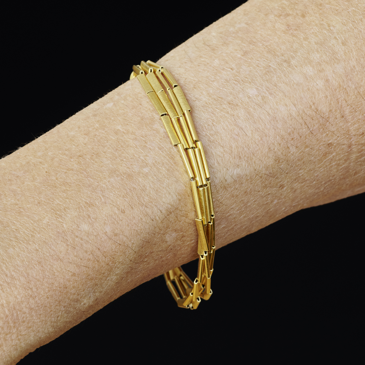 Schlankes Halmarmband aus Silber, feingoldplattiert, getragen am Handgelenk vor schwarzem Hintergrund. Das Armband wirkt elegant und filigran, ideal als feines Schmuckstück für festliche und persönliche Anlässe.