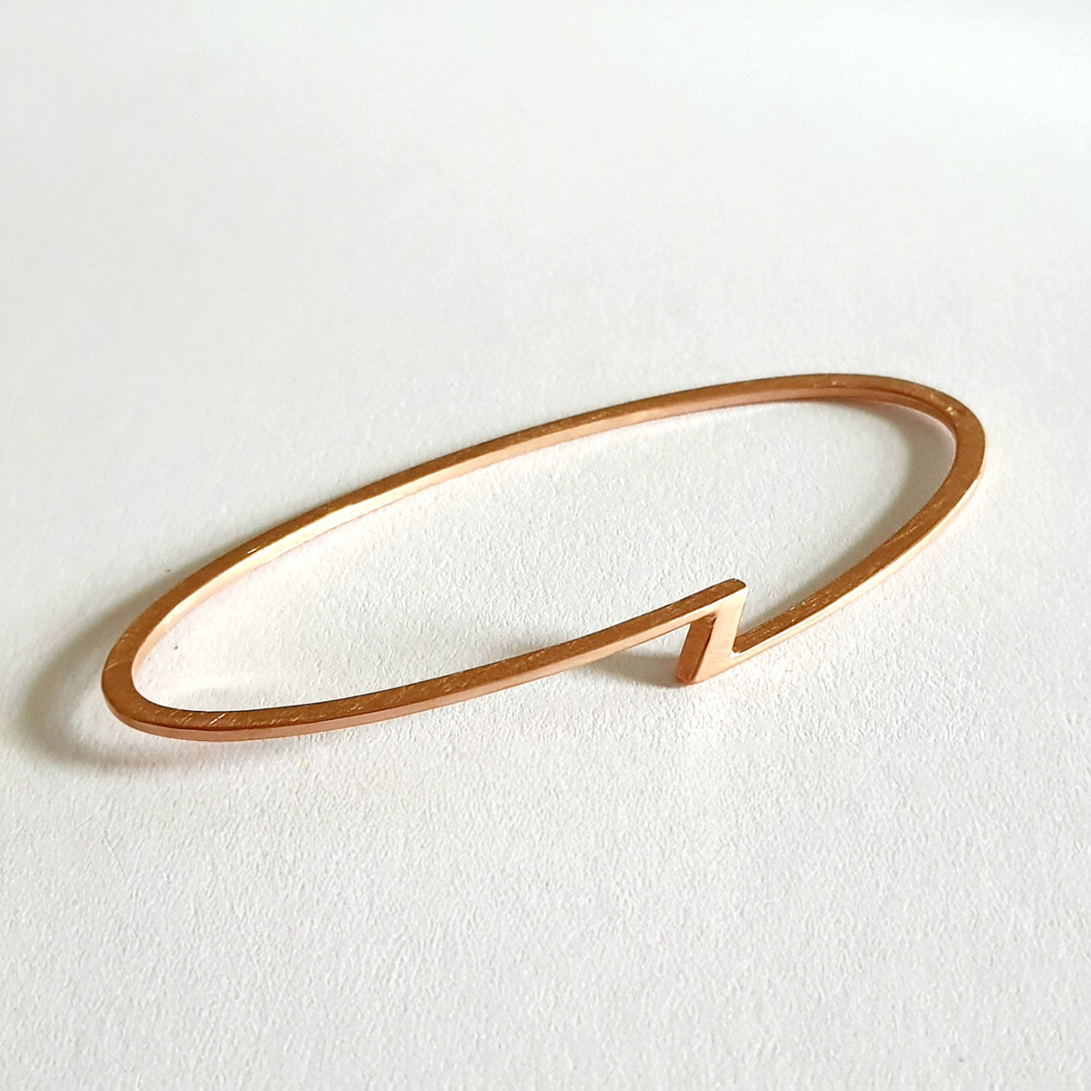 Ein eleganter Armreif der ZEIT-Jubiläumsedition, in einer minimalistischen Form mit einem dezenten goldenen Glanz. Der Armreif liegt auf einem hellen Hintergrund.