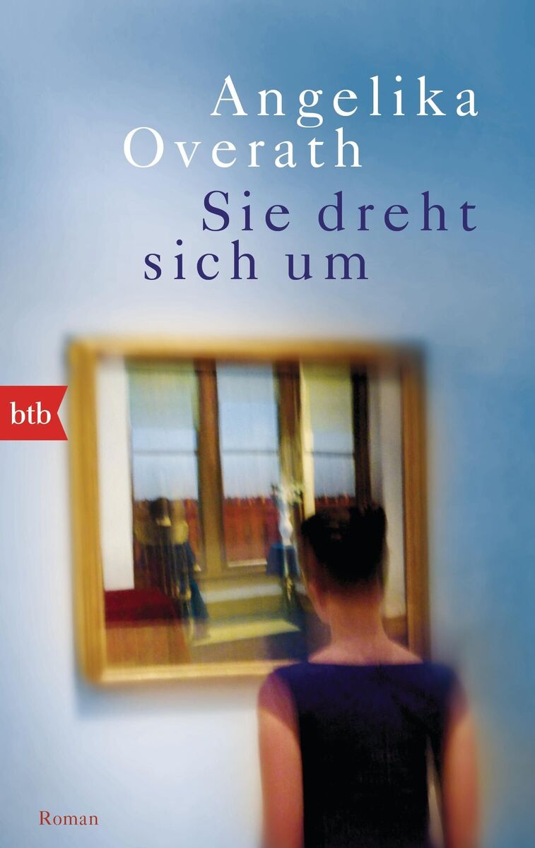 Cover des Buches 'Sie dreht sich um' von Angelika Overath. Der Umschlag zeigt die Rückenansicht einer Frau vor einem unscharfen Spiegelbild, das einen Türrahmen und zwei Fenster in einem Raum mit Holzboden reflektiert. Oben sind der Titel und der Name der Autorin in blauen und lilafarbenen Buchstaben zu sehen.