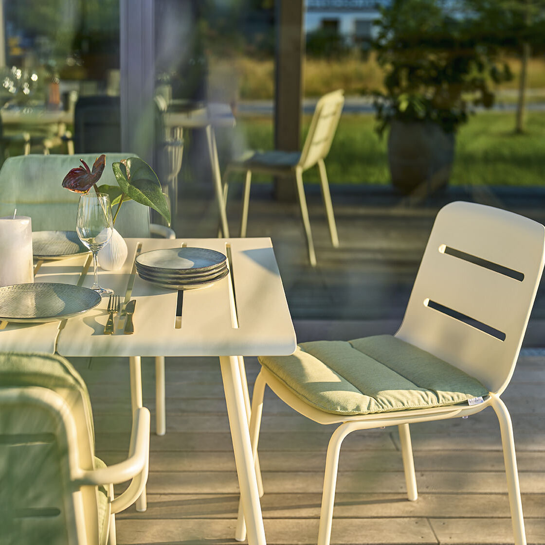 Essbereich mit einem modernen weißen Tisch und weißen Stühlen, darunter ein Stuhl »VAPIO« basic. Der Essbereich steht auf einer Terrasse, und im Hintergrund sind Grünflächen und weitere Sitzgelegenheiten zu sehen.