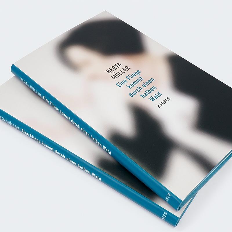 Zwei Bücher mit verschwommenem Cover. Der Titel lautet "Herta Müller: Eine Fliege kommt durch einen halben Wald".