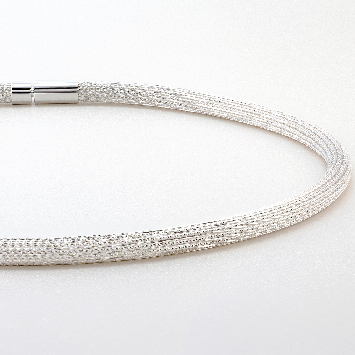 Das Bild zeigt das Collier »Milanaise« von Menard, ein handgefertigtes Schmuckstück aus feinen Silberdrähten. Die Oberfläche ist glatt und das Geflecht rund, mit einem silberfarbenen Verschluss. Es wirkt edel und modern auf einem hellen Hintergrund.