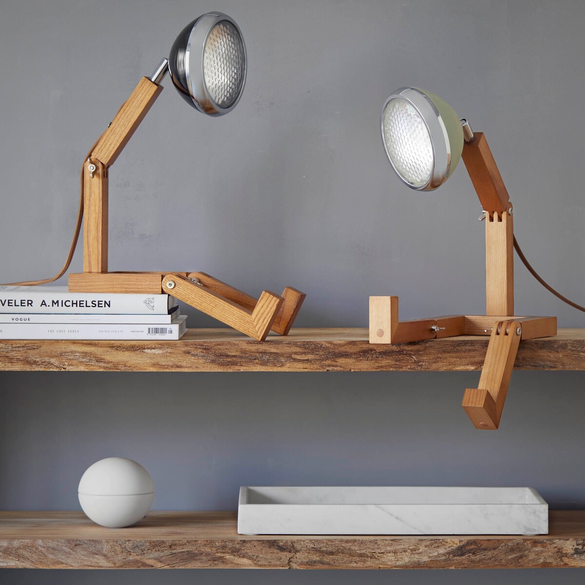 Zwei Tischlampen der Marke 'Mr. Wattson' auf einem Holzregal, die teilweise aus Holz und Metall bestehen. Eine Lampe steht aufrecht, während die andere hingesetzt ist. Sie haben einen retro-modernen Designstil.