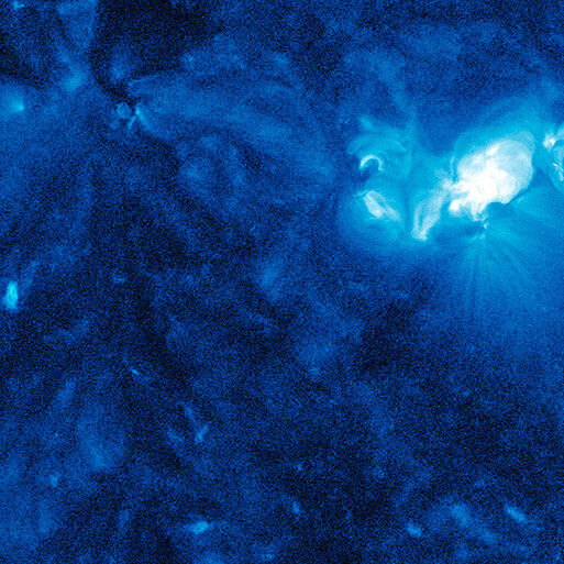 Künstlerisches Bild von Katharina Sieverding mit dem Titel »Die Sonne um Mitternacht schauen SDO/NASA«, 2017. Das Bild zeigt eine in Blau gehüllte Darstellung der Sonne mit einem intensiven Leuchten im Zentrum. Es hat weltraumbasierte visuelle Elemente und vermittelt eine mystische, astronomiebezogene Atmosphäre.