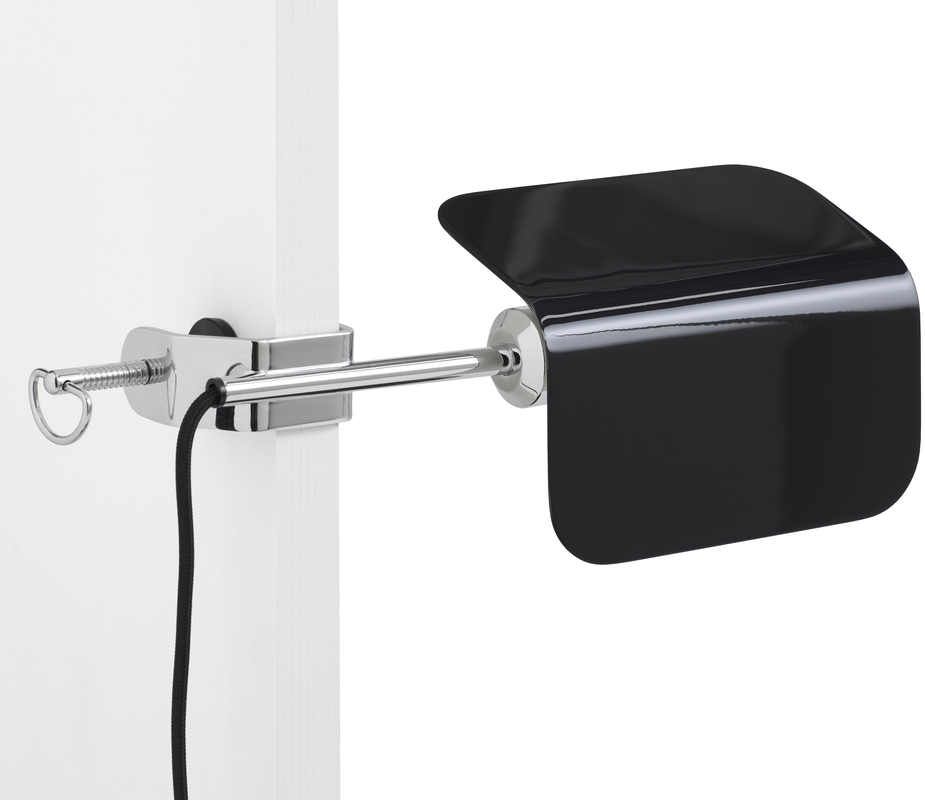 Eine moderne Lampe mit schwarzem Schirm und silbernem Befestigungsclip, der an einem weißen Brett befestigt ist. Ein Kabel führt von der Lampe weg.