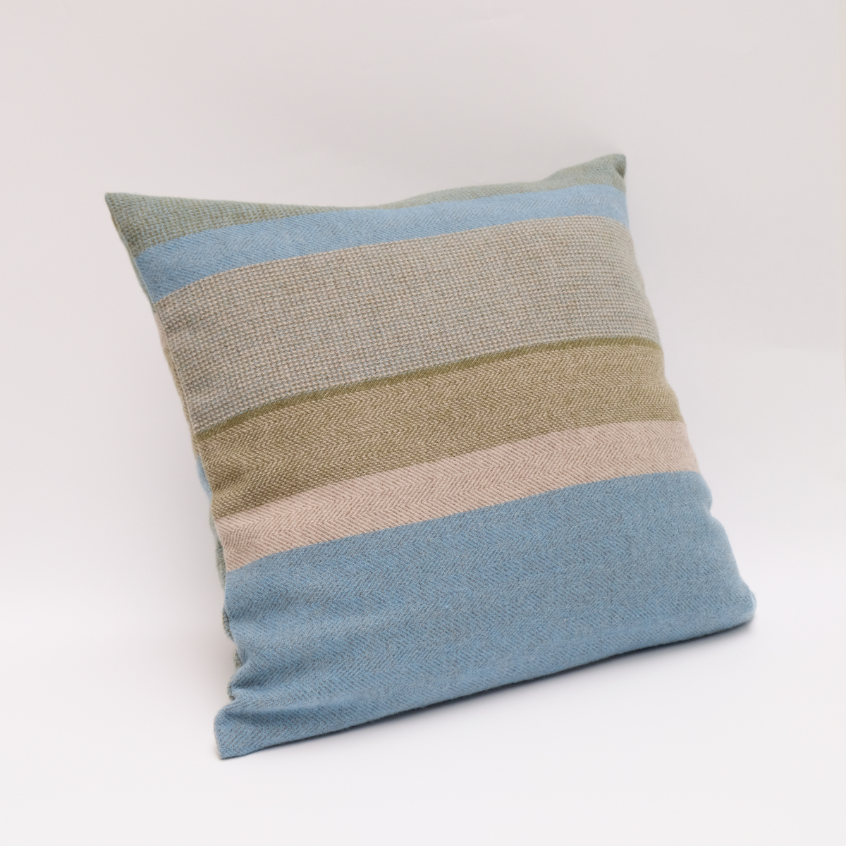 Ein Kissen aus der Kollektion Merionkissen FreeFlowMind mit Streifen in Blau, Grün und Beige auf einem sandfarbenen Hintergrund. Perfekt für moderne Wohnräume geeignet.