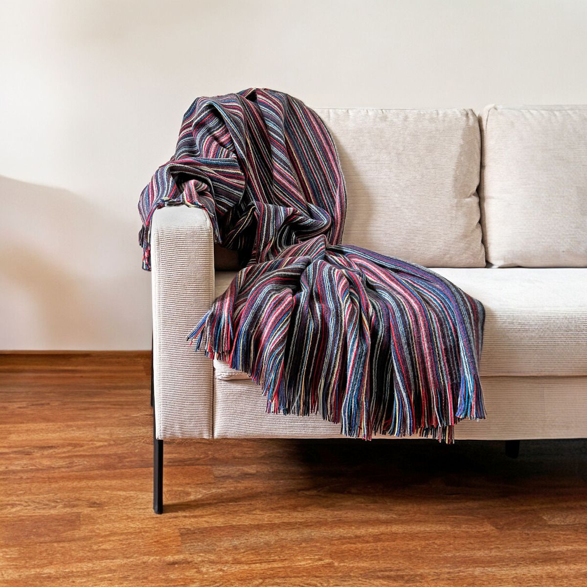 Eine bunte Wolldecke mit Streifenmuster liegt auf einem hellen Sofa in einem Wohnzimmer mit Holzboden, geschaffen für eine gemütliche Atmosphäre.