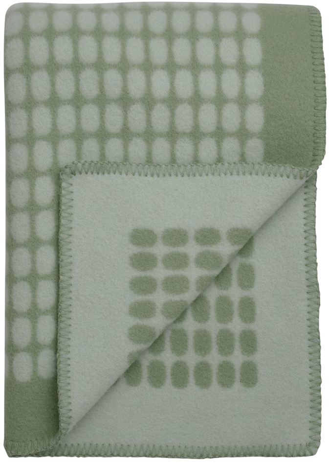 Grüne Lammwolldecke mit einem geometrischen Muster, das aus rechteckigen Formen in Weiß besteht. Die Decke ist gefaltet und zeigt sowohl das äußere als auch das innere Muster.