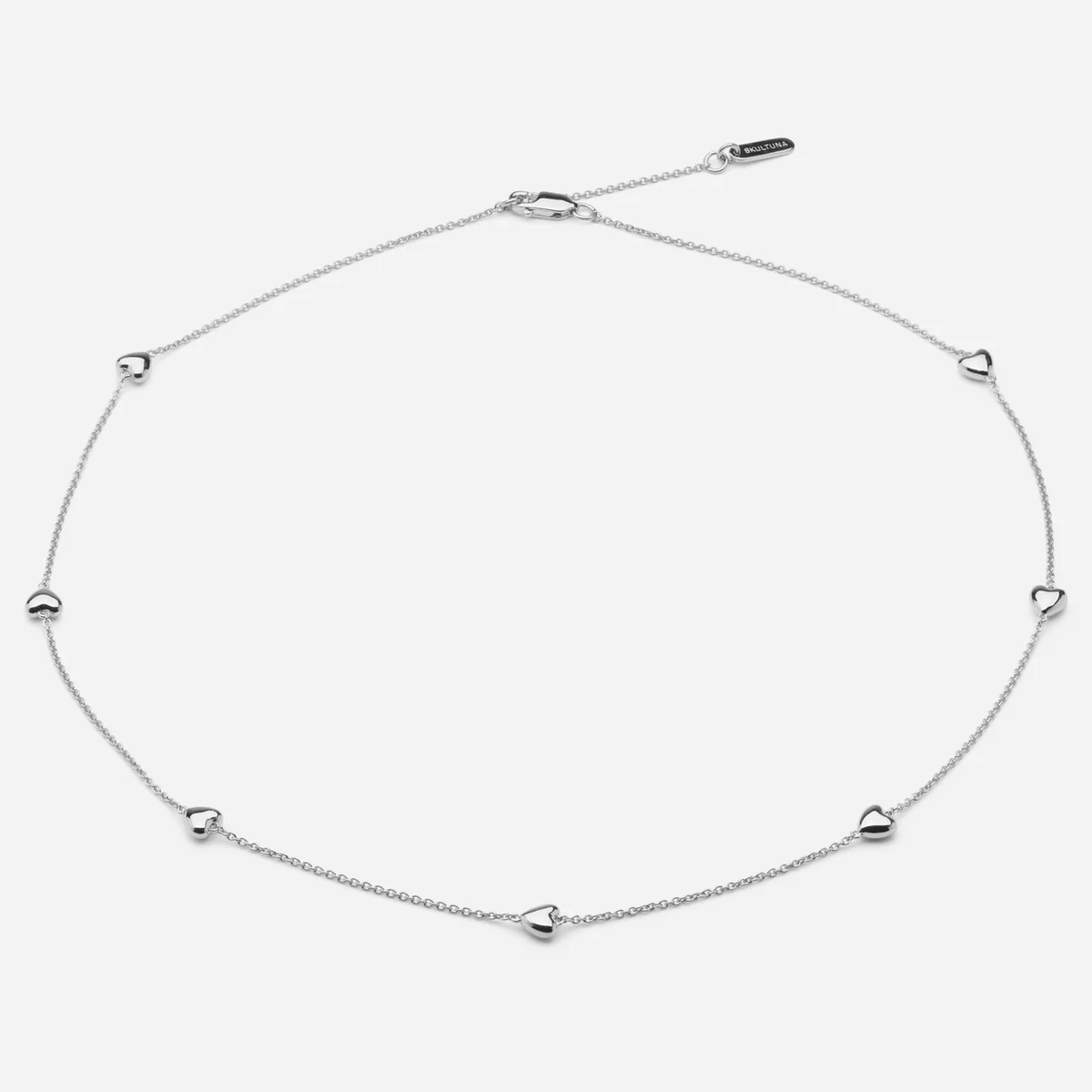 Das Bild zeigt eine zarte Collier-Halskette aus Sterling-Silber der Marke SKULTUNA MESSINGSBRUK. Die feine Kette ist gleichmäßig mit kleinen, herzförmigen Anhängern versehen und wirkt modern und elegant. Der Schmuck liegt auf hellem, neutralem Hintergrund.