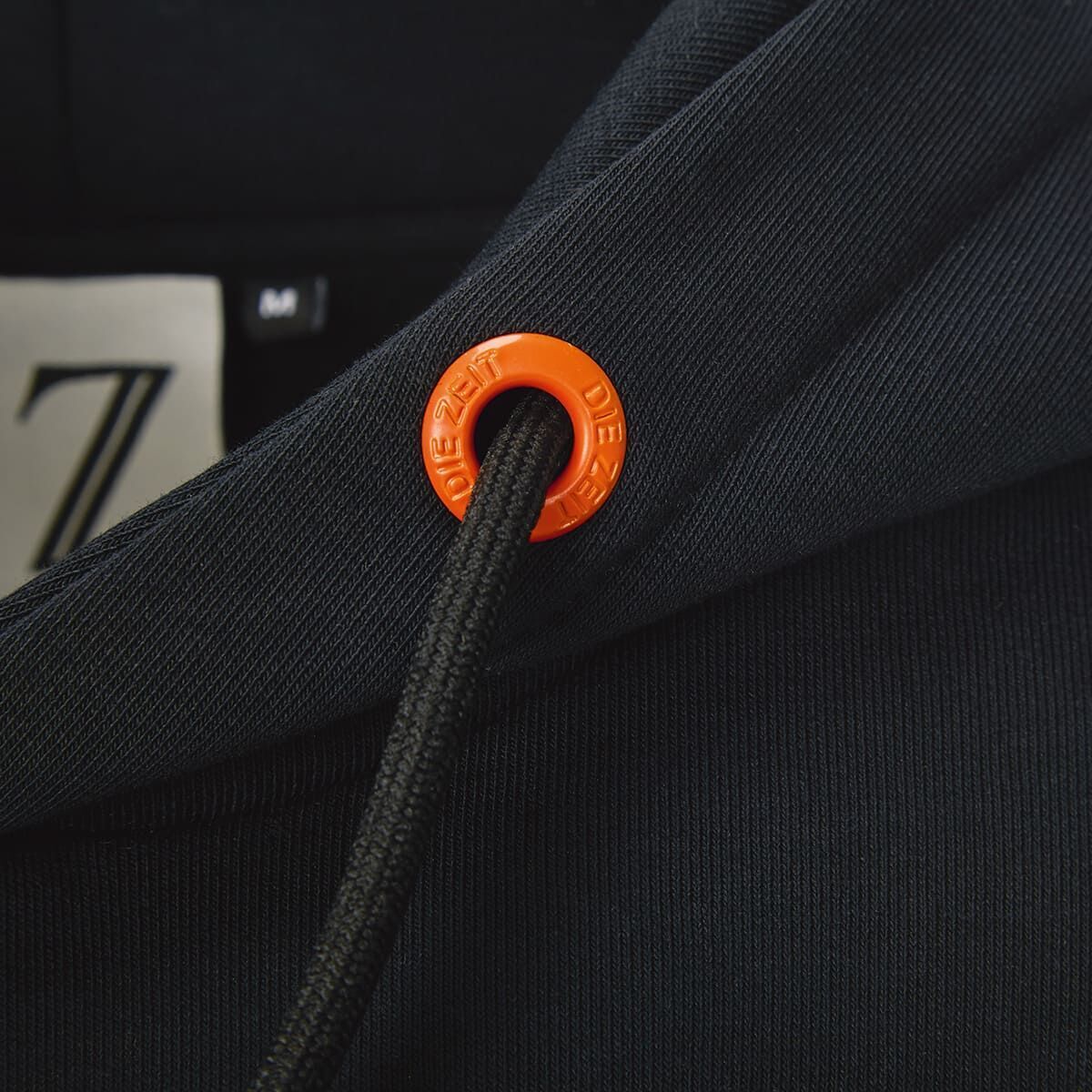 Detailansicht eines schwarzen Hoodies mit orangenen Kordelenden, Teil der ZEIT-Kollektion.
