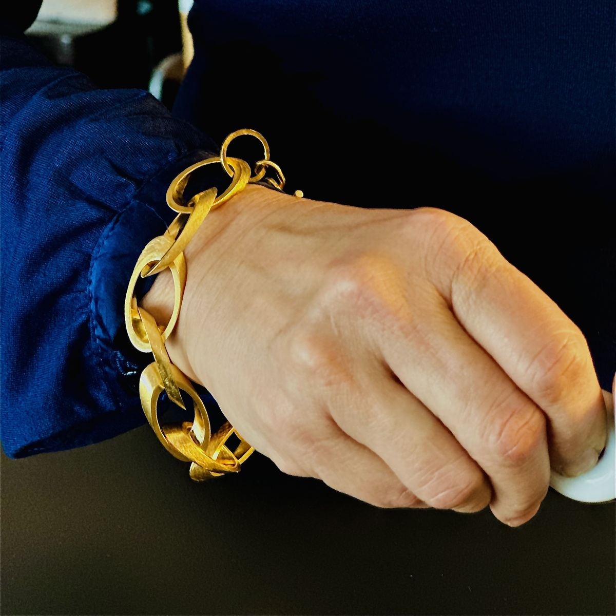 Nahaufnahme eines feingoldplattierten silbernen Armbands am Handgelenk einer Person in einem blauen Oberteil.
