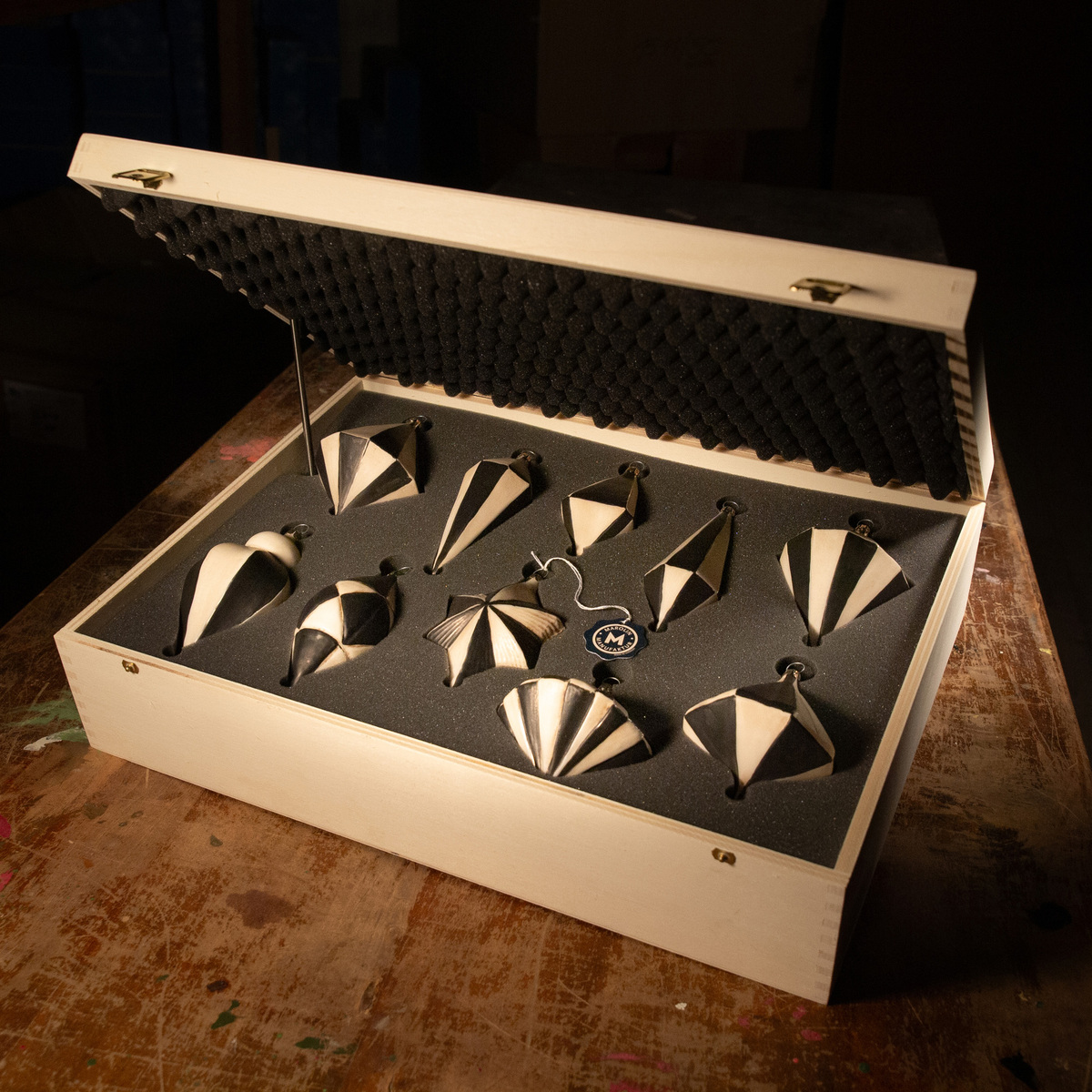Ein Set von 10 schwarzen und weißen Christbaumkugeln in geometrischen Formen, sicher in einer hellen Holzkiste verpackt.