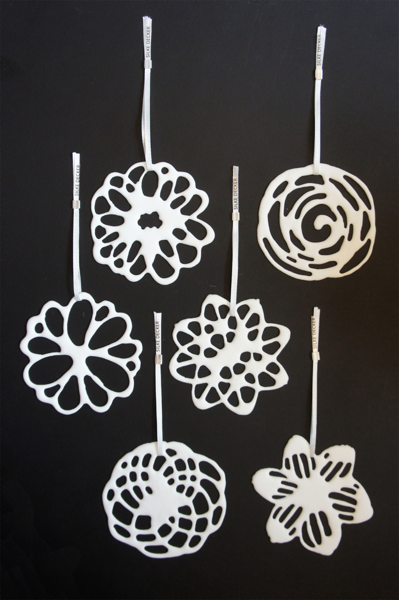 Ein Set bestehend aus sechs weißen, hängenden Porzellanblüten vor einem schwarzen Hintergrund. Jede Blüte hat ein einzigartiges und filigranes Design, das an handgefertigte Kunstwerke erinnert.