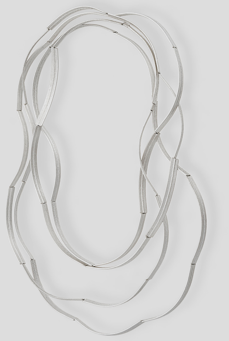 Filigrane, dreifach gelagerte Kette »Bogen« aus feinem Silber, gestaltet von Franziska Rappold. Der Schmuck besteht aus sanft gebogenen Elementen, die zu einer eleganten, schlichten Halskette verbunden sind. Das Design wirkt modern und zeitlos; Hintergrund einfarbig hellgrau.