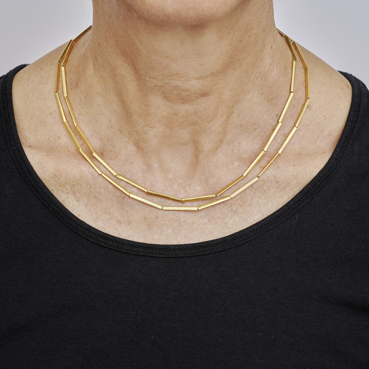 Eine elegante, feingoldplattierte Halmkette aus Silber ist doppelt um den Hals einer Person gelegt. Die Gliederkette hat eine moderne, minimalistische Optik und wird zu einem schlichten schwarzen Oberteil getragen.