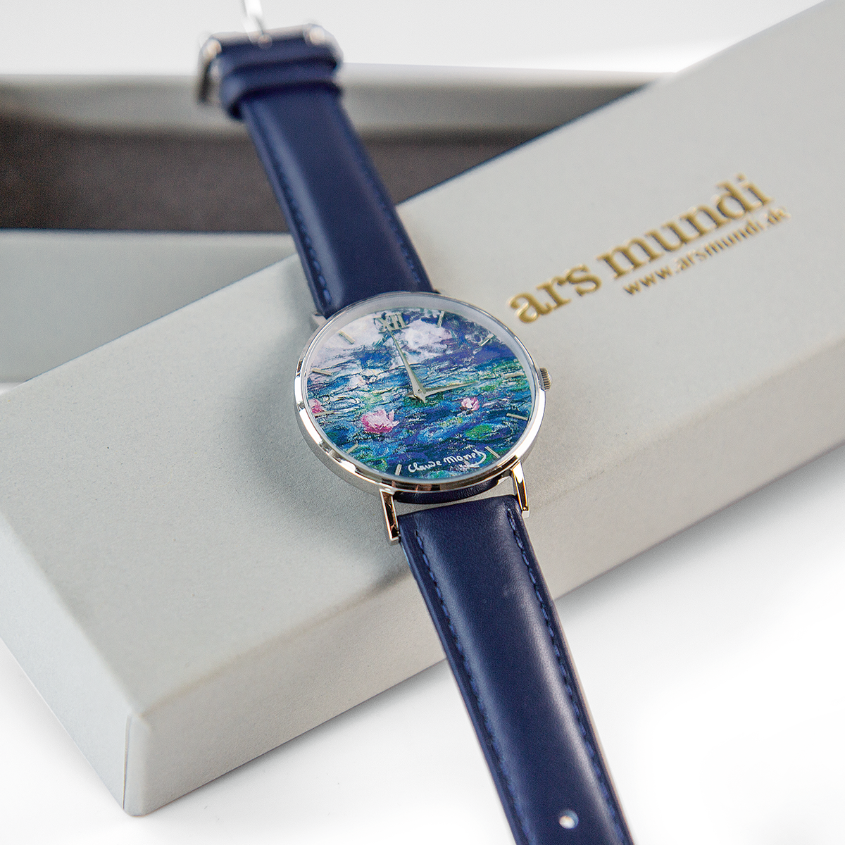 Künstler-Armbanduhr »Monet - Les Nymphéas« mit einem Zifferblatt, das Monets Seerosenmotiv zeigt. Die Uhr hat ein blaues Armband und wird in einer schicken Verpackung präsentiert.
