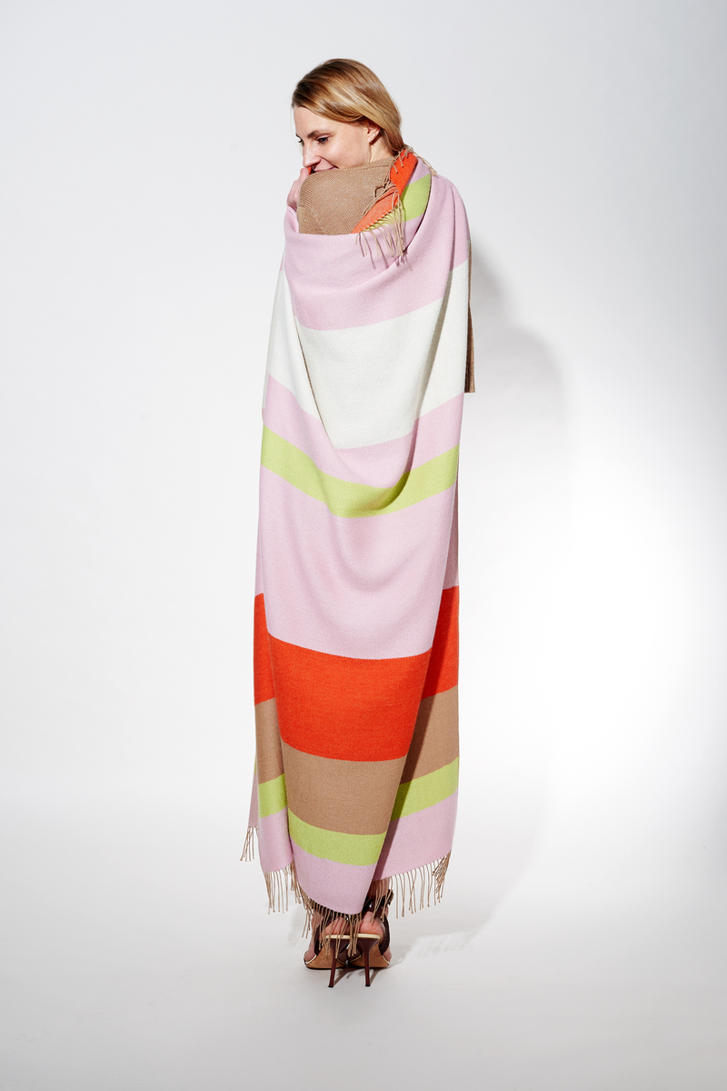 Frau trägt ein Cape aus Alpaka-Wolle mit Streifen in Rosa, Weiß, Grün, Orange und Beige.