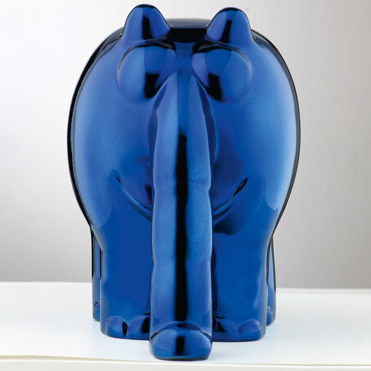 Eine Skulptur des Ottifanten von Otto Waalkes in einer hochglänzenden metallic-blauen Oberfläche. Die Figur steht auf einem hellen Untergrund vor neutralem Hintergrund. Der Ottifant ist von hinten zu sehen, mit dickem Rüssel und rundlichen Formen.
