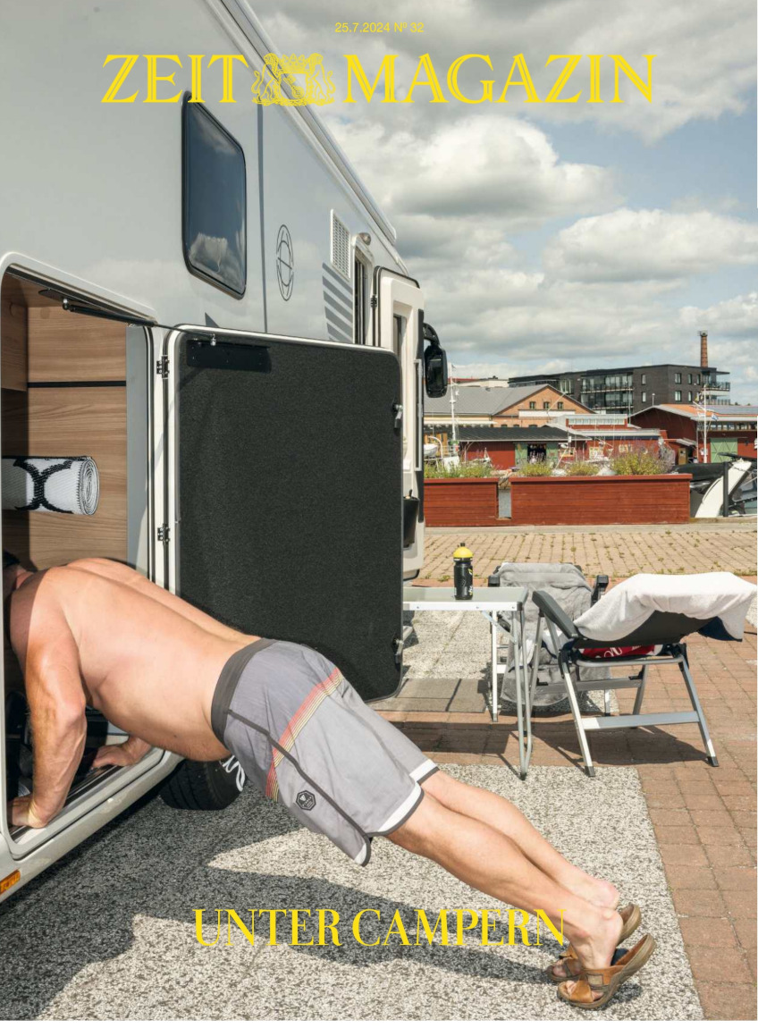Ein Mann in grauen Shorts und braunen Sandalen macht Übungen vor einem weißen Wohnmobil auf einem Campingplatz. Ein Tisch und ein Stuhl stehen in der Nähe. Im Hintergrund sieht man einen blauen Himmel mit weißen Wolken sowie einige Gebäude und Bäume.