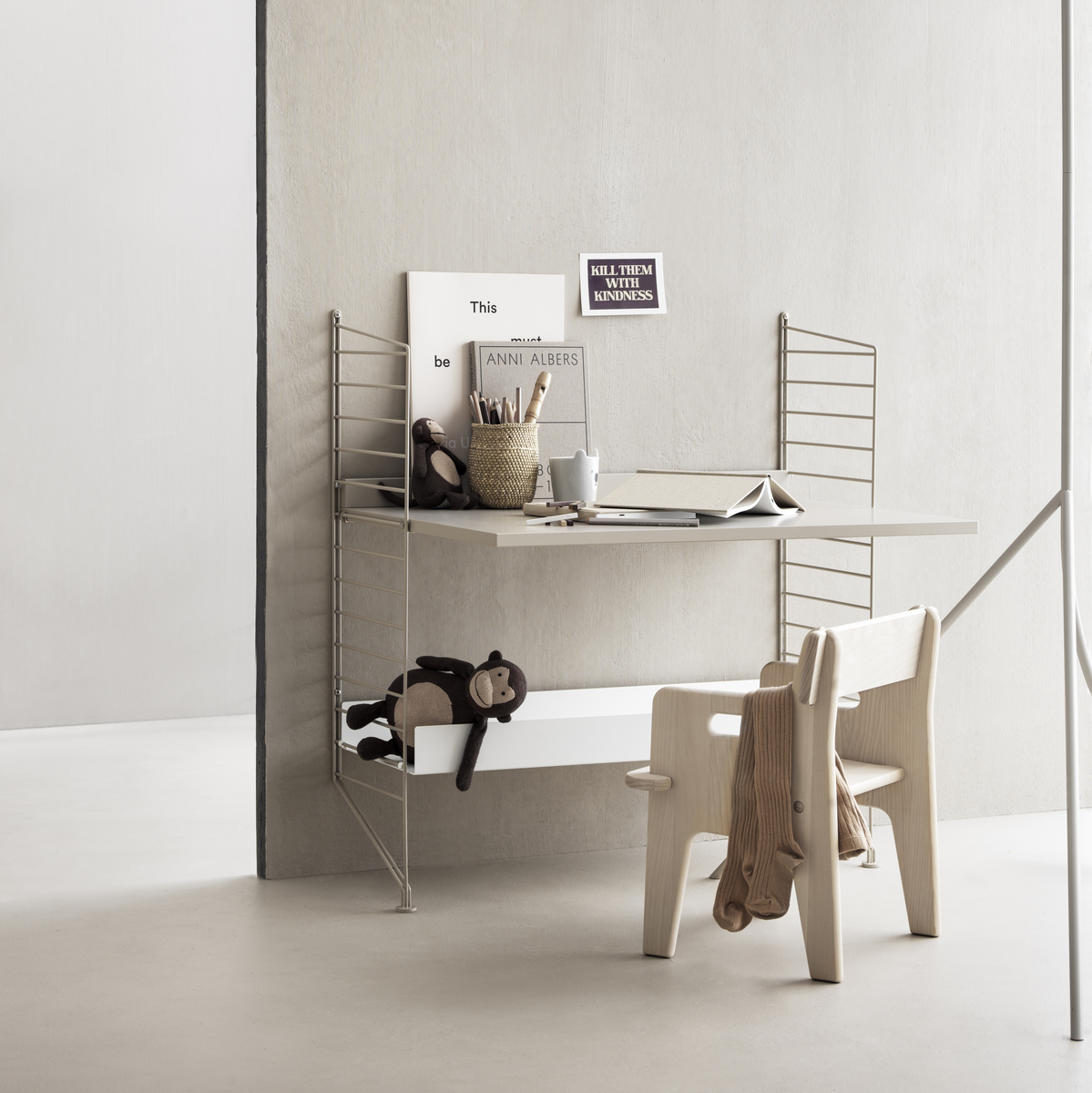 Ein stilvoller Kinderzimmer-Schreibtisch mit einem Schreibtischstuhl und Spielzeug. Der Schreibtisch ist mit Büchern, Farben und Schreibutensilien ausgestattet und steht vor einer beige Wand. Die Umgebung ist minimalistisch und funktional gestaltet, ideal für das Lernen und kreative Aktivitäten von Kindern.