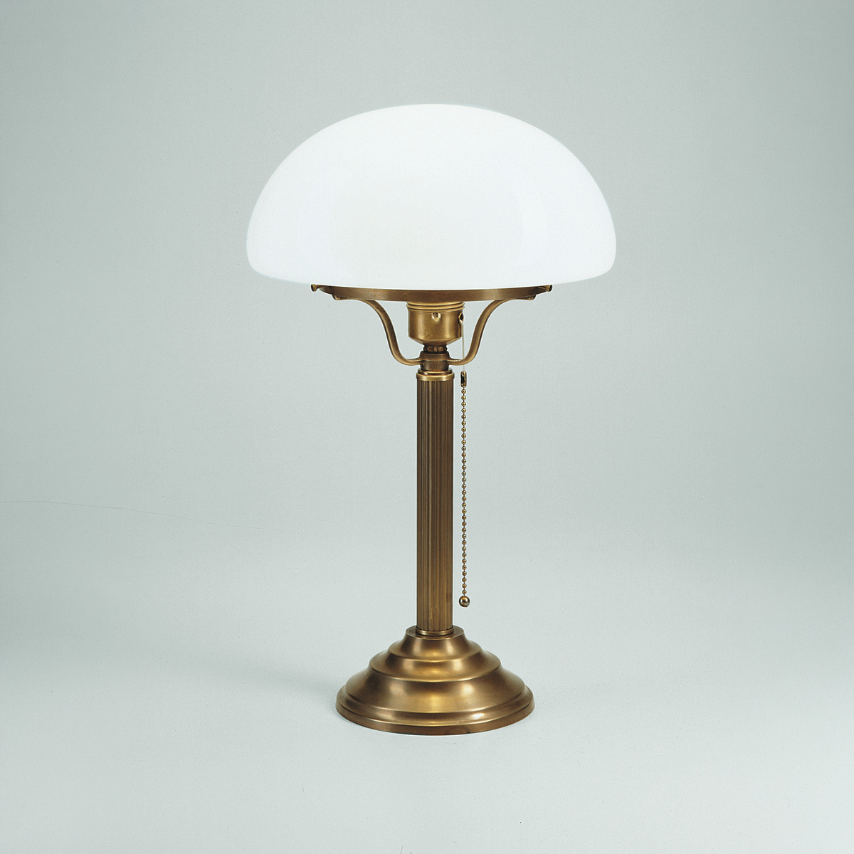 Elegante Jugendstil-Pilzleuchte »Berlin« von Ars mundi aus Berliner Messing mit rundem Standfuß und Kettenschalter. Der Schirm aus mundgeblasenem, weißem Opalglas bildet einen Kontrast zum gold-bronzefarbenen Gestell. Zeitloses Design für stilvolle Räume.