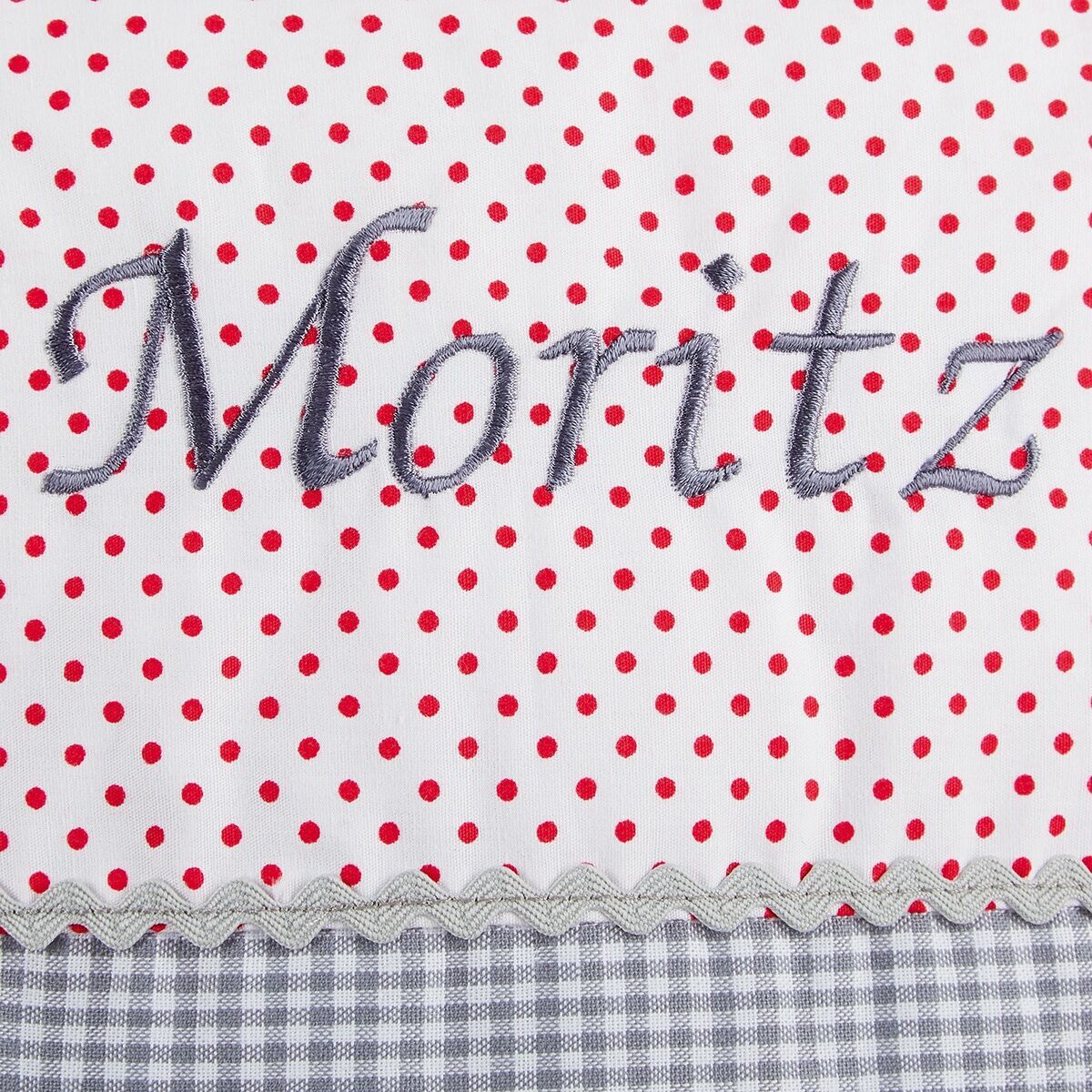 Ein personalisiertes Kissen mit dem Namen 'Moritz' auf einem weißen Hintergrund mit roten Punkten und grauem kariertem Saum.
