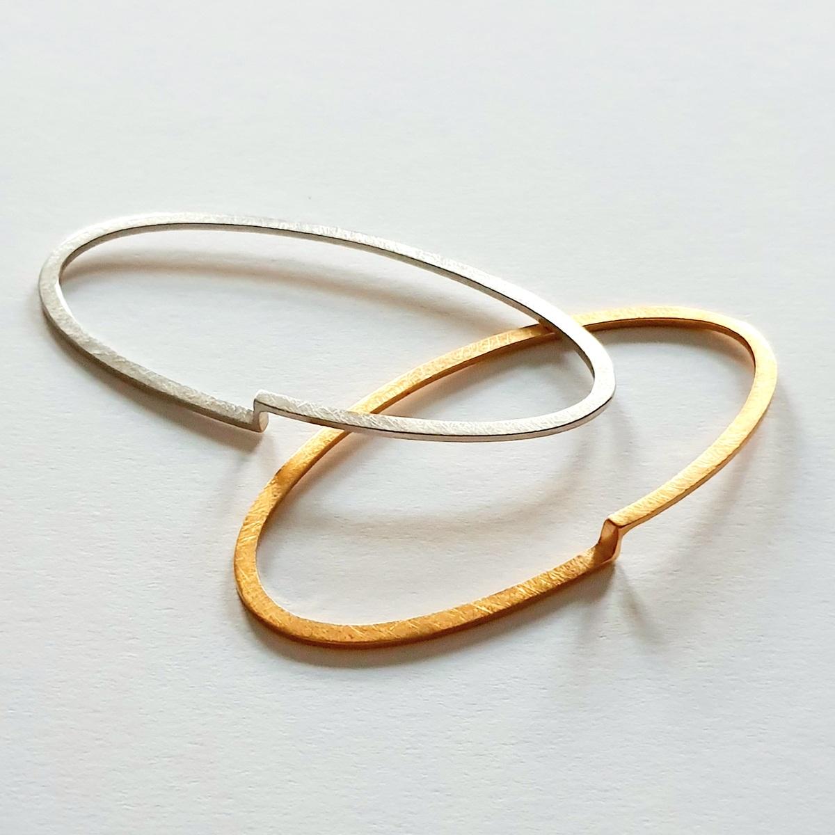 Zwei schlichte Armreifen auf hellem Hintergrund, einer in Gold- und einer in Silberoptik, in minimalistischem Design.
