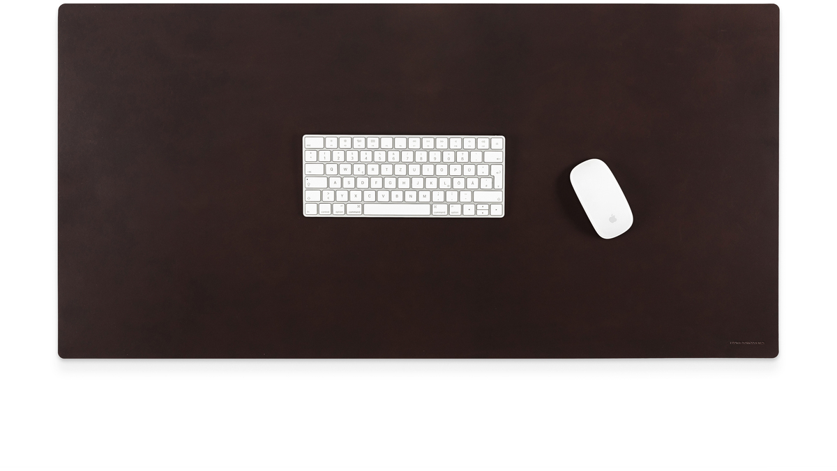 Braune Schreibtischunterlage aus Lederoptik, darauf eine weiße Tastatur und eine weiße Maus, alles auf einem modernen, minimalistischen Arbeitsplatz arrangiert.