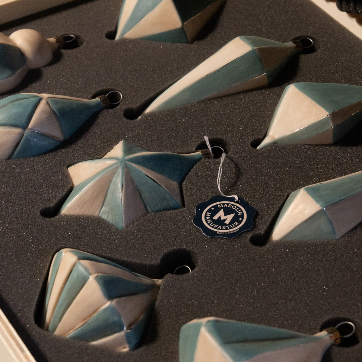 Christbaumkugeln im Set von zehn Stück in verschiedenen geometrischen Formen, verpackt in einer schwarzen Schaumstoffbox. Die Farben der Kugeln sind hauptsächlich Blau und Weiß.