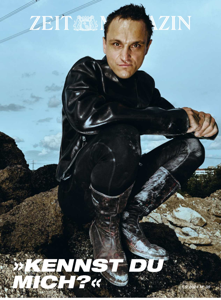 Titelbild des ZEIT Magazins Ausgabe 38/2024. Zu sehen ist ein Mann in schwarzer Kleidung mit Stiefeln, sitzend auf einer Steinlandschaft. Im Hintergrund ist ein Himmel zu sehen. Auf dem Cover steht die Frage: 'Kennst du mich?'