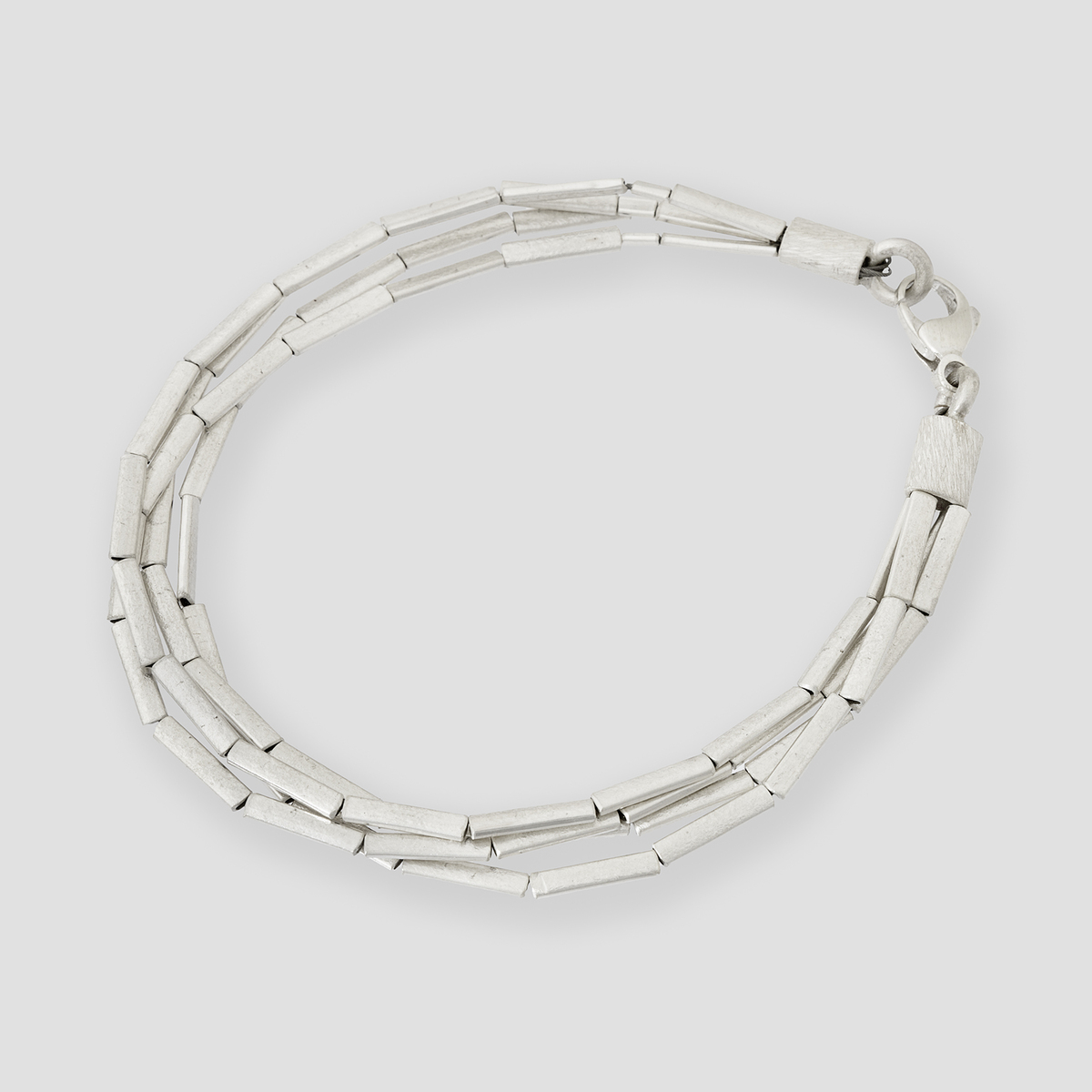 Abgebildet ist ein feines Halmarmband aus glänzendem Silber mit schlichten, röhrenförmigen Gliedern und einem Verschluss, liegend vor einem hellgrauen, neutralen Hintergrund.