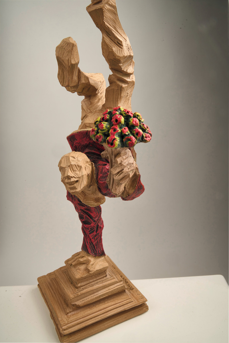 Figurative Skulptur von Roman Johann Strobl in Holzoptik, zeigt eine akrobatische Figur mit Blumenstrauß, auf einem verzierten Sockel stehend. Die Skulptur ist detailliert und in den Farben Holzbraun, Rot und Grün gestaltet.